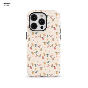 May include: A phone case with a cream background featuring a repeating pattern of string lights in various colors and small star shapes. The case has a black camera ring and the text "THE ONE CASE" in the upper left corner.