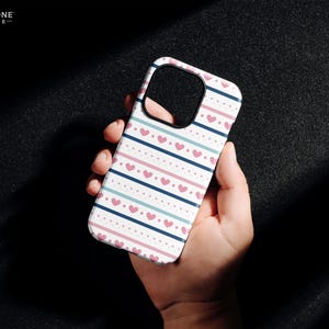 May include: A white phone case with a pink and blue striped pattern and pink hearts. The case is designed for an iPhone.