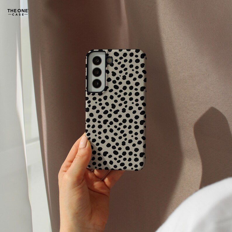 May include: A smartphone case with a beige background and a pattern of black spots. The case has a rectangular shape with rounded corners and a camera cutout. The brand name "THE ONE CASE" is printed in the upper left corner.