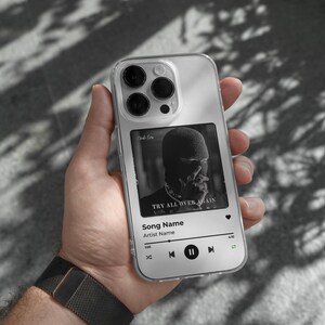 May include: A clear phone case with a black and white album cover design. The album cover features a person wearing a black mask and the text "Try All Over Again". The phone case also has a music player interface with the text "Song Name" and "Artist Name".