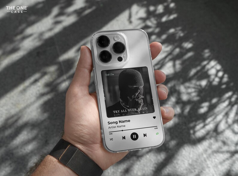 May include: A clear phone case with a black and white album cover design. The album cover features a person wearing a black mask and the text "Try All Over Again". The phone case also has a music player interface with the text "Song Name" and "Artist Name".