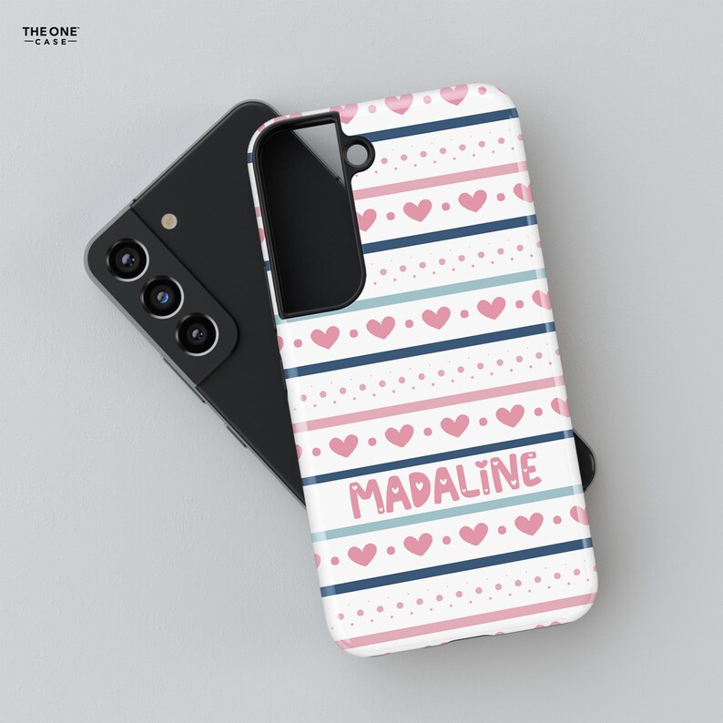 May include: A white phone case with a pink and blue striped pattern and pink hearts. The name "MADALINE" is written in pink letters on the case.