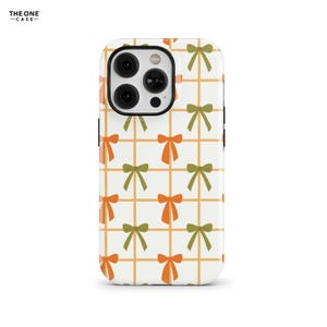 Puede incluir: Funda de teléfono blanca con un patrón repetido de lazos naranjas y verdes sobre una cuadrícula naranja. La funda del teléfono tiene un módulo de cámara negro y el texto "THE ONE -CASE-" en la esquina superior izquierda.