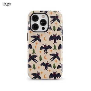 Puede incluir: Una funda de teléfono con un patrón repetido de criaturas negras parecidas a polillas con ojos rojos, árboles verdes, lunas crecientes y estrellas sobre un fondo beige. La funda tiene un recorte para la cámara y el texto "THE ONE -CASE-".