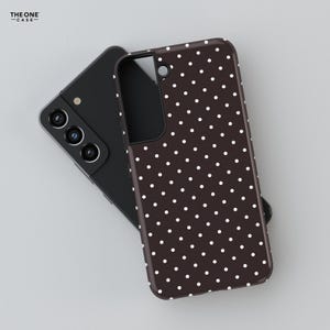 May include: A black smartphone with a brown phone case featuring a white polka dot pattern. The phone case is covering the back of the phone. The text "THE ONE -CASE-" is in the upper left corner.