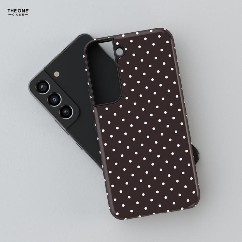 May include: A black smartphone with a brown phone case featuring a white polka dot pattern. The phone case is covering the back of the phone. The text "THE ONE -CASE-" is in the upper left corner.