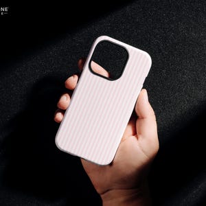 Pu&ograve; includere: Una custodia per telefono bianca con un motivo a righe verticali rosa. La custodia ha un ritaglio nero per la fotocamera ed &egrave; tenuta in mano. Il testo "THE ONE -CASE-" si trova nell'angolo in alto a sinistra.