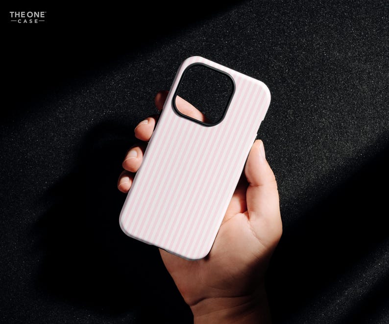 Pu&ograve; includere: Una custodia per telefono bianca con un motivo a righe verticali rosa. La custodia ha un ritaglio nero per la fotocamera ed &egrave; tenuta in mano. Il testo "THE ONE -CASE-" si trova nell'angolo in alto a sinistra.