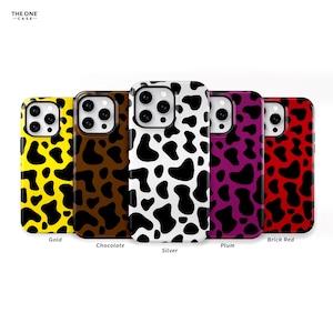 Puede incluir: Cinco fundas para teléfono diferentes con un diseño de estampado de vaca. Las fundas son de color dorado, chocolate, plateado, ciruela y rojo ladrillo.