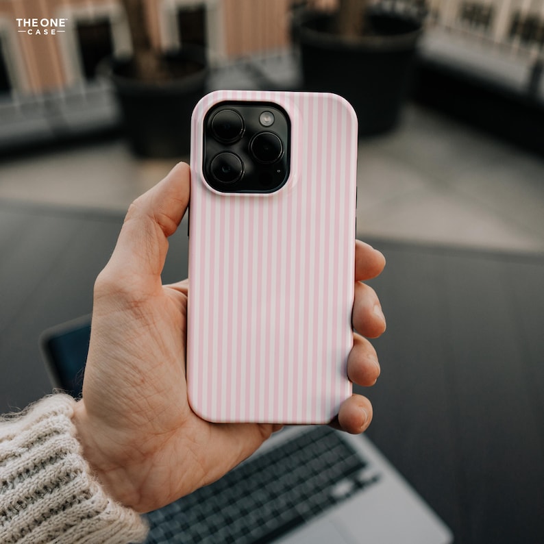 Pu&ograve; includere: Una custodia per telefono a righe rosa e bianche con un modulo fotocamera nero. La custodia presenta un motivo a righe verticali. Il testo "THE ONE CASE" si trova nell'angolo in alto a sinistra. La custodia del telefono &egrave; tenuta in mano.