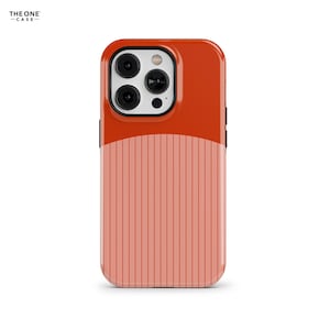Puede incluir: Una funda para smartphone con diseño bicolor, que presenta una sección superior en naranja oscuro sólido y una sección inferior en color coral claro con rayas verticales. El área de la cámara es blanca con tres lentes negras.