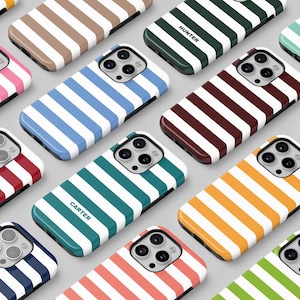 Op de afbeelding: Een verzameling kleurrijke gestreepte telefoonhoesjes met verschillende namen die op elk hoesje zijn gedrukt. De hoesjes zijn in een rasterpatroon op een wit oppervlak gerangschikt.
