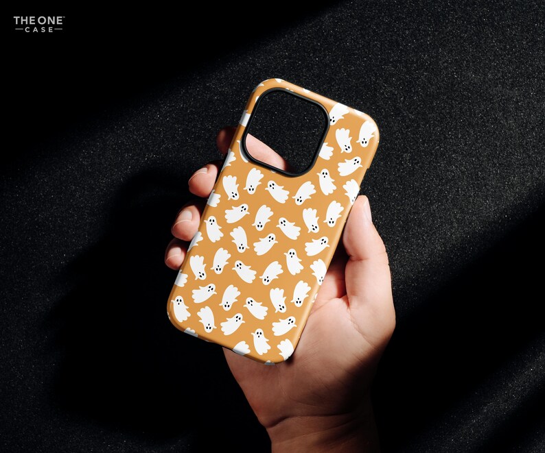 May include: A phone case with a repeating pattern of white ghost illustrations on a tan background. The case has a black border and the text "THE ONE -CASE-" in the upper left corner.