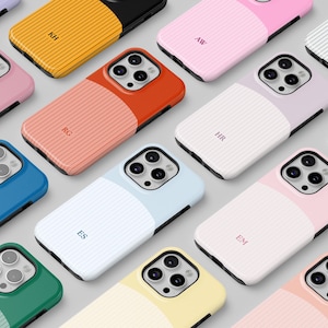 Puede incluir: Una colección de fundas para smartphone con un diseño bicolor, textura acanalada en un lado y acabado liso en el otro. Cada funda muestra un monograma de dos letras y un recorte para un sistema de cámara de triple lente.