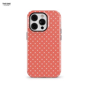 Puede incluir: Una funda de teléfono rosa coral con un patrón de lunares blancos. La funda está diseñada para un iPhone.