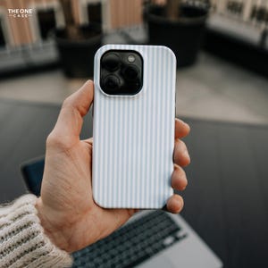 Pode incluir: Capa de smartphone com padr&atilde;o de listras brancas e azul claro. A capa tem um m&oacute;dulo de c&acirc;mera preto e &eacute; segurada em uma m&atilde;o. O texto "THE ONE CASE" est&aacute; no canto superior esquerdo.