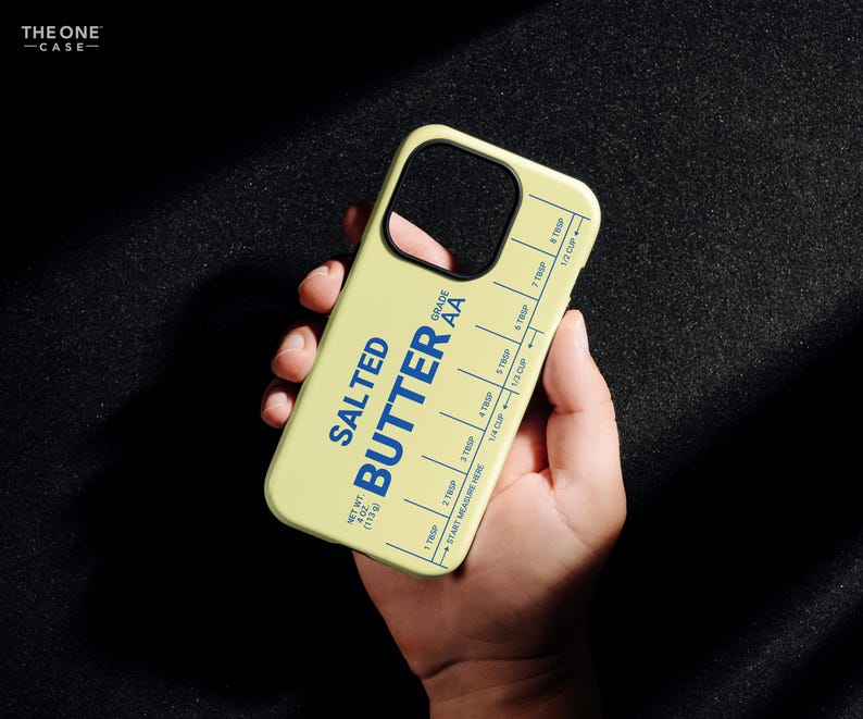 Pu&ograve; includere: Una custodia per telefono giallo chiaro con le parole "SALTED BUTTER" in blu, insieme a segni di misurazione. La custodia ha anche il testo "GRADE AA" e "NET WT 113g". La custodia del telefono &egrave; tenuta in una mano.