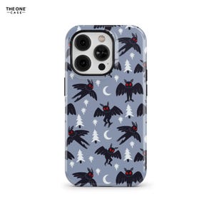 Puede incluir: Una funda de teléfono con un patrón repetido de criaturas negras parecidas a polillas con ojos rojos, árboles blancos, lunas crecientes y estrellas sobre un fondo azul claro. La funda tiene un módulo de cámara negro y el texto "THE ONE -CASE-" en la esquina superior izquierda.