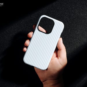 Pode incluir: Capa de telefone azul claro com um padr&atilde;o listrado, segurada na m&atilde;o. A capa tem um recorte preto para a c&acirc;mera e o texto "THE ONE -CASE-" no canto superior esquerdo. O fundo &eacute; escuro.