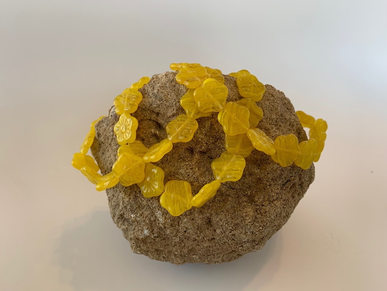 May include: A strand of yellow flower-shaped beads wrapped around a rough, brown rock.