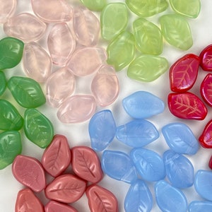 May include: Assortment of glass leaf beads in various colors, including pink, green, red, blue, and brown. The beads are all in the shape of a leaf and have a slightly textured surface.
