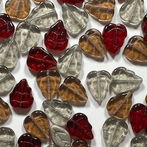 May include: Assortment of glass leaf beads in red, brown, and clear colors. The beads are shaped like leaves with a hole in the center for stringing.
