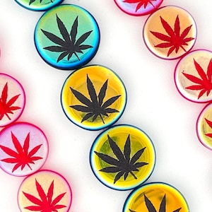 May include: Assortment of round, iridescent glass beads with a black marijuana leaf design. The beads are in various colors, including red, yellow, green, and blue.