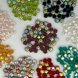 May include: Assortment of iridescent star-shaped glass beads in various colors, including green, black, brown, clear, gold, red, and blue.