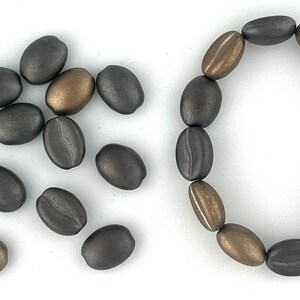 May include: A collection of dark gray and bronze coffee bean shaped beads. Some beads are loose and others are strung together to form a bracelet.