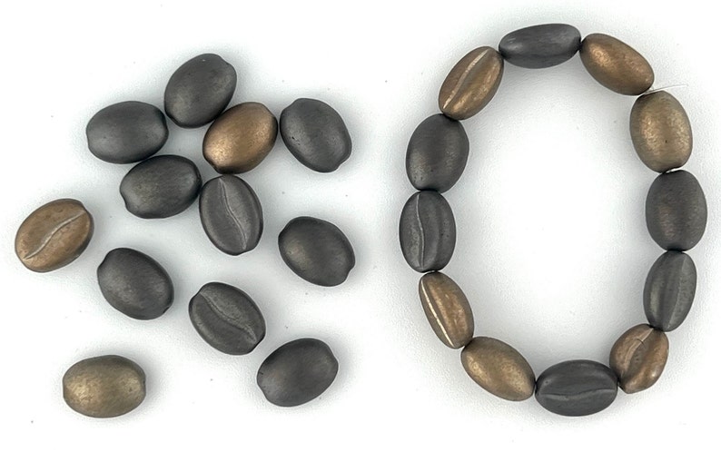 May include: A collection of dark gray and bronze coffee bean shaped beads. Some beads are loose and others are strung together to form a bracelet.