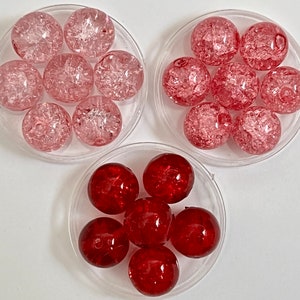 May include: Three sets of glass beads in different colors. The first set is pink and white, the second set is pink and white, and the third set is red. The beads are all round and have a textured surface.