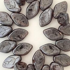 May include: A collection of dark gray glass beads with a leaf design. The beads are arranged in a circle on a white background.