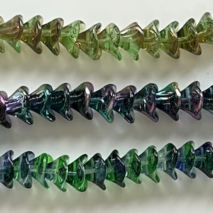 May include: Three strands of iridescent glass beads in shades of green, teal, and purple. The beads have a unique, flared shape, strung together in a row. The beads are likely for jewelry making or craft projects.