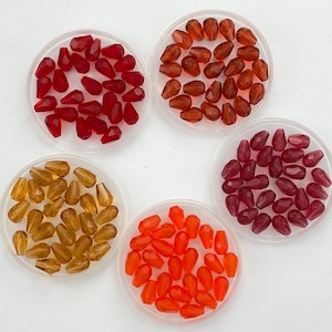 May include: Five small bowls filled with teardrop-shaped glass beads in various shades of red, orange, and amber.