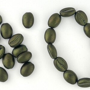 May include: A collection of green coffee bean shaped beads. Some beads are arranged in a circle, while others are scattered on a white surface.