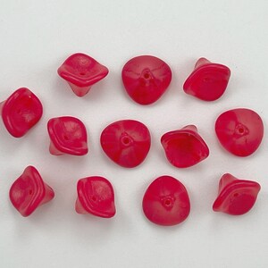May include: A collection of 12 bright pink glass beads with a unique flower shape. The beads have a hole in the center for stringing.