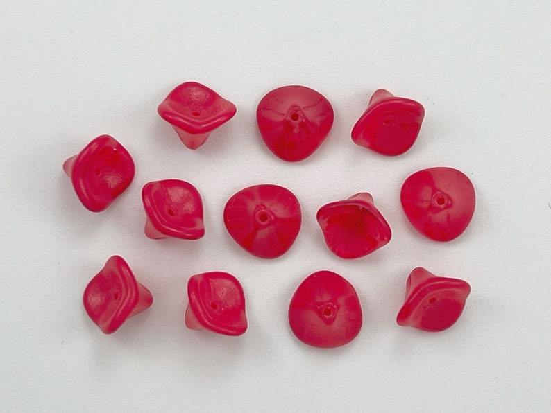 May include: A collection of 12 bright pink glass beads with a unique flower shape. The beads have a hole in the center for stringing.