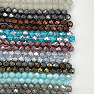 May include: Rows of faceted beads in various colors, including black, iridescent, clear, silver, bronze, turquoise, burgundy, and gray. The beads are strung together, creating a textured and colorful display, perfect for jewelry making.