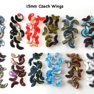 May include: Various colors of 15mm Czech glass wings, including iridescent, black, red, and blue. These crescent-shaped beads are arranged in rows on a white surface. The text "15mm Czech Wings" is at the top.