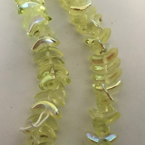 May include: Close-up of two strands of pale yellow, iridescent glass beads. The beads are leaf-shaped and strung together with silver-colored wire. The beads have a slight shimmer and are arranged in a repeating pattern.