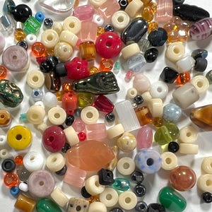 May include: A collection of various beads in different shapes, sizes, and colors. The beads include round, oval, and irregular shapes in shades of red, pink, yellow, green, and cream. Some beads have holes, while others are solid.