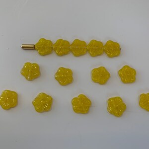 May include: A collection of yellow flower-shaped buttons. The buttons are arranged in a line and a semi-circle.