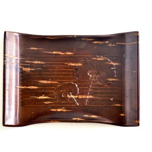 May include: A rectangular, dark brown wooden tray with a curved design. The tray features a carved floral design with gold accents. The tray is likely used for decorative purposes or serving small items.