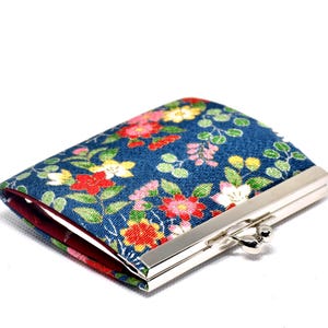 May include: A small rectangular coin purse featuring a blue fabric exterior with a colourful floral pattern of red, yellow, and white blossoms and green leaves. The purse has a silver-toned metal kiss-lock clasp and a solid dark red interior lining.