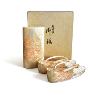 Könnte beinhalten: Ein Set traditioneller japanischer Geta-Sandalen mit passendem zylindrischen Behälter und Box. Die Geta und der Behälter weisen ein Blumenmuster in Gold und Orange auf. Die Box hat japanischen Text.