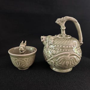 以下が含まれることがあります： 龍のモチーフが施された、セーラーカラーのセラミックティーセット。 小さなカップと、龍の頭の取っ手と注ぎ口が付いたティーポットが含まれています。 ティーポットとカップは、花柄とスクロール模様で装飾されています。