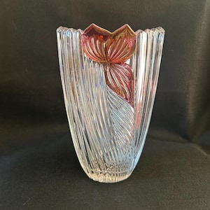May include: A clear glass vase with a textured, ribbed design. The vase has a red, glass flower design on the front.