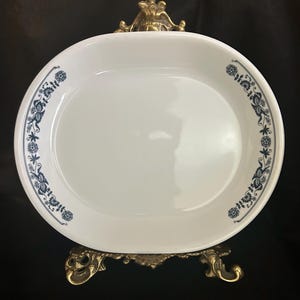 Puede incluir: Plato ovalado blanco para servir con un diseño floral azul en el borde. El plato se exhibe sobre un soporte decorativo de metal dorado. El patrón floral incluye flores y hojas estilizadas.