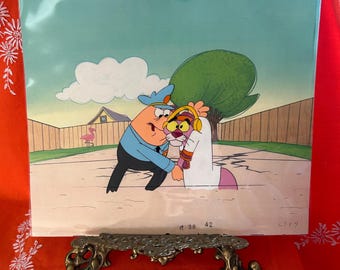 May include: Animation cel featuring two cartoon characters in a street scene. One character, a police officer in a blue uniform, is interacting with a pink panther-like character wearing headphones. A fence, tree, and house are in the background.