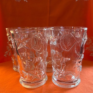 May include: A set of clear, embossed drinking glasses. Each glass has a repeating pattern of stars, shells, and nautical designs. The glasses are cylindrical with a flared base, ideal for serving drinks. Each glass is approximately 15 cm tall.